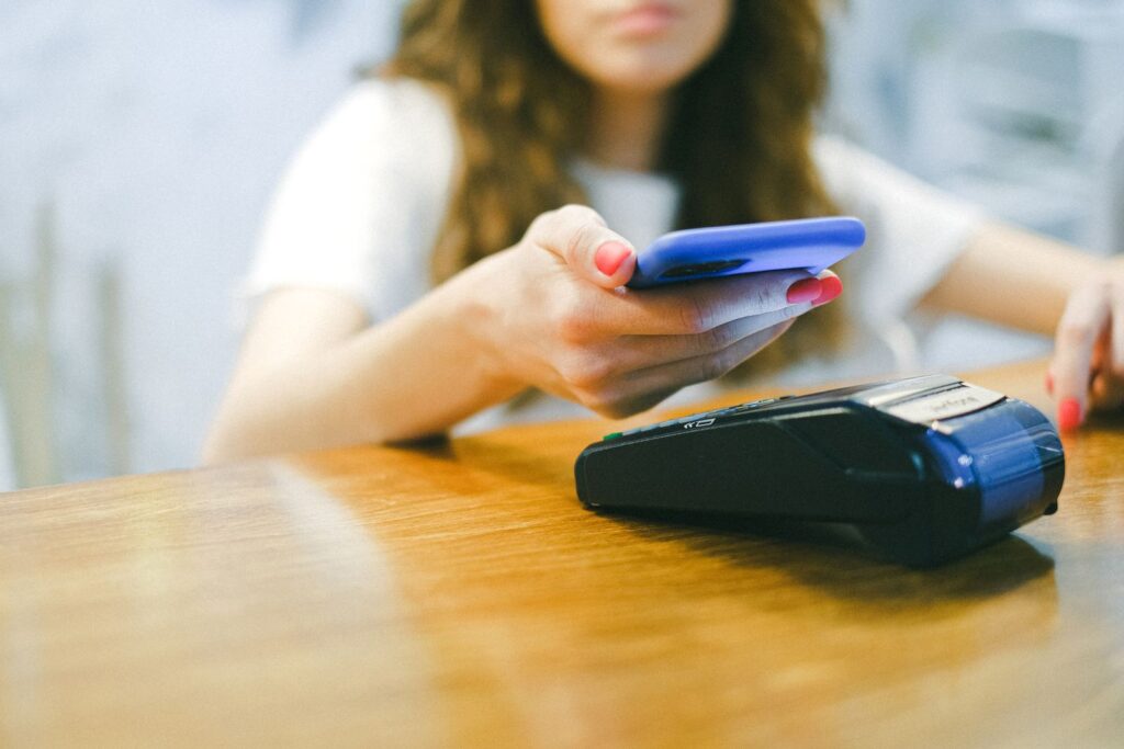 A person tapping a smartphone on a contactless card reader at a checkout to tap to pay