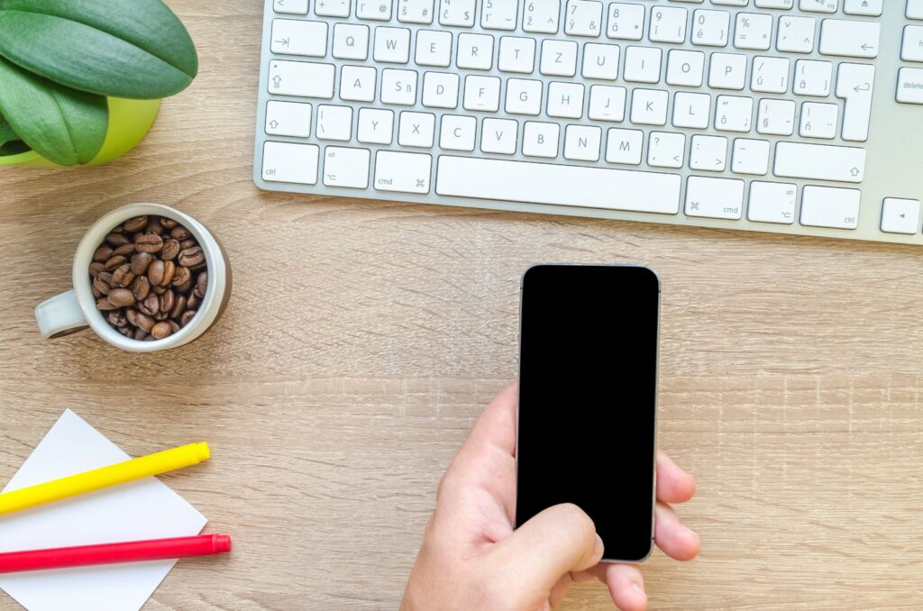 A hand holding a smartphone at a desk while reviewing app permissions