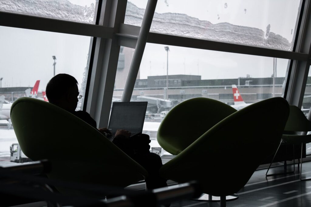 A traveler working on a laptop in an airport lounge with planes outside, a reminder about public wifi safety
